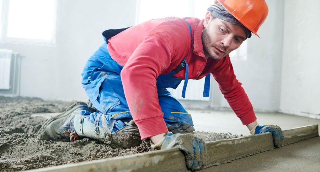 Arbeiter, der einen Zementboden in einem Raum mit Estrich verlegt